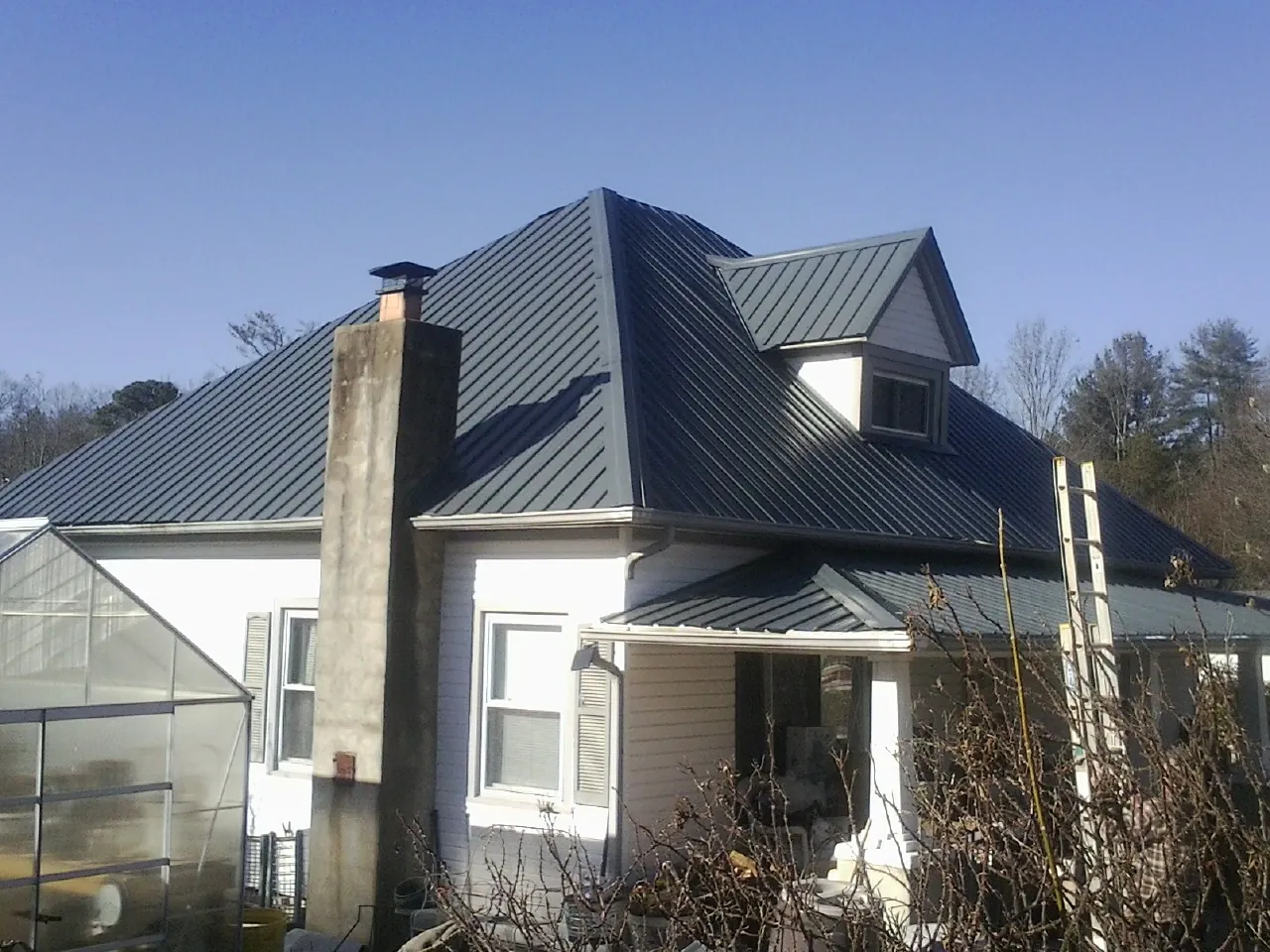 Dark blue standing seam metal roof on a white farmhouse with dormer — Slate & Tile Roof Repair by Roofing Brothers in Mantoloking