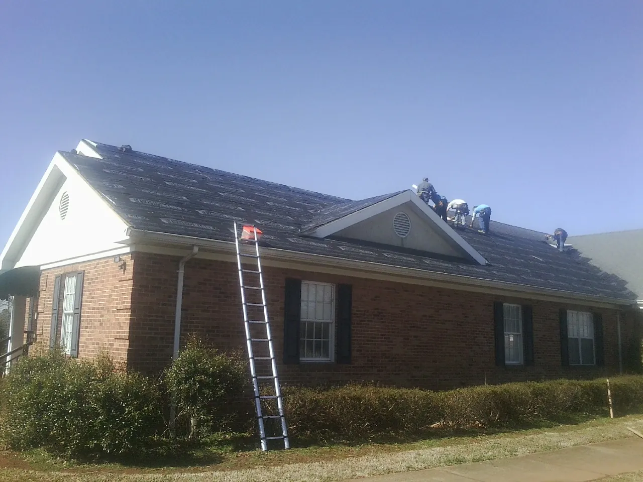 Crew tearing shingles off a brick ranch roof with a ladder set — Emergency Roof Repair work by our crew in Mantoloking