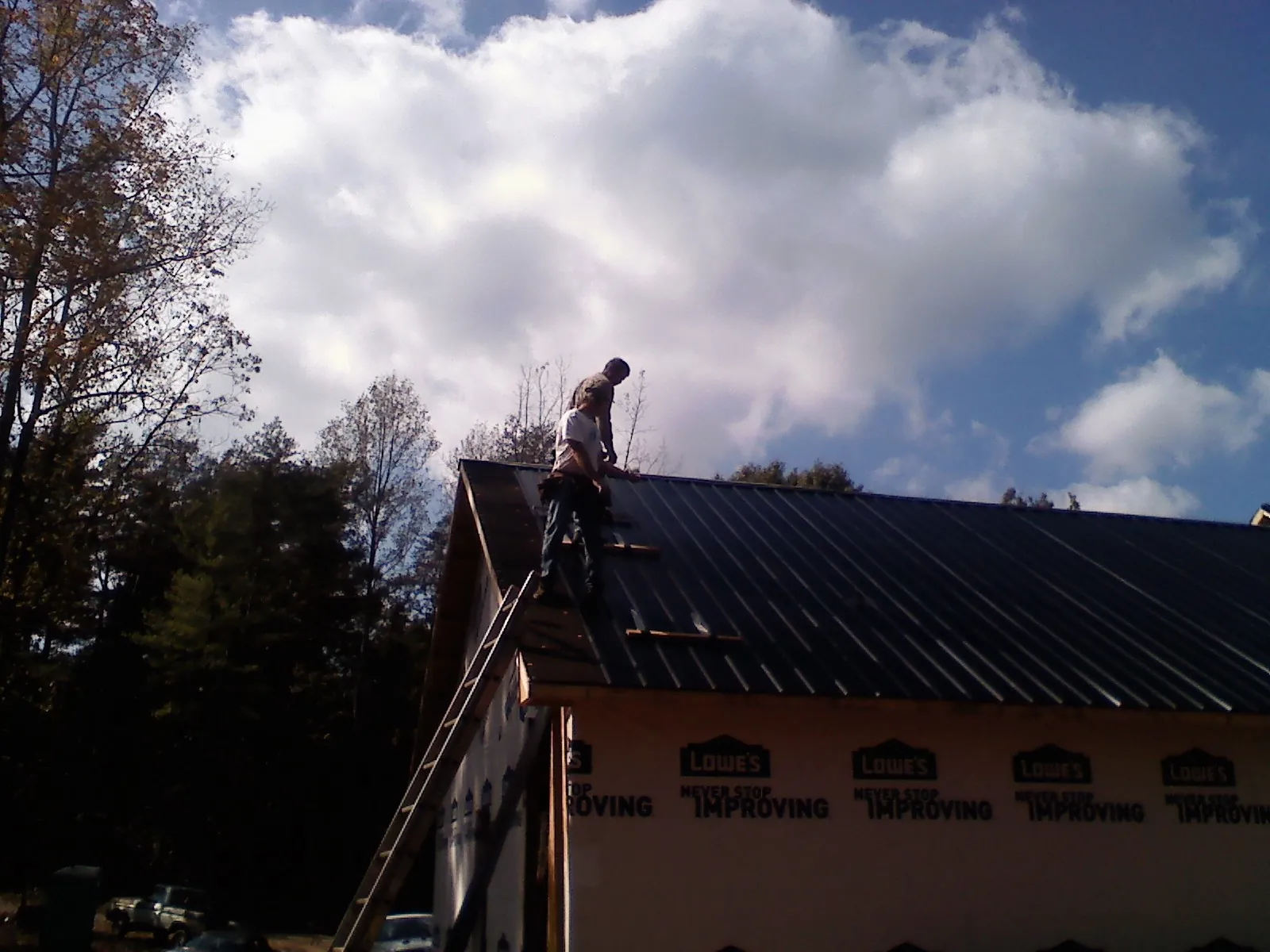 Roofer fastening dark metal panels high against a cloudy sky, from a Roof Inspection job in Mantoloking