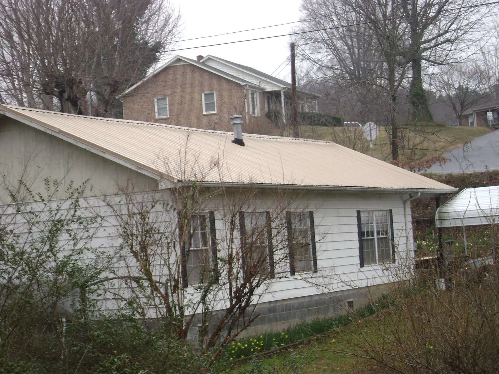 Tan metal roof on a white sided house set into a hillside — Commercial Roofing by Roofing Brothers in Mantoloking